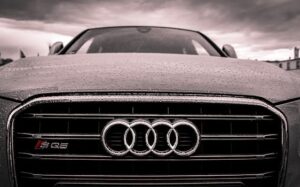 Close-up of a rain-covered Audi car grille showcasing luxury and elegance under cloudy skies.