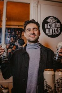 Smiling man with unique drink cans at a lively event with mirror decoration.